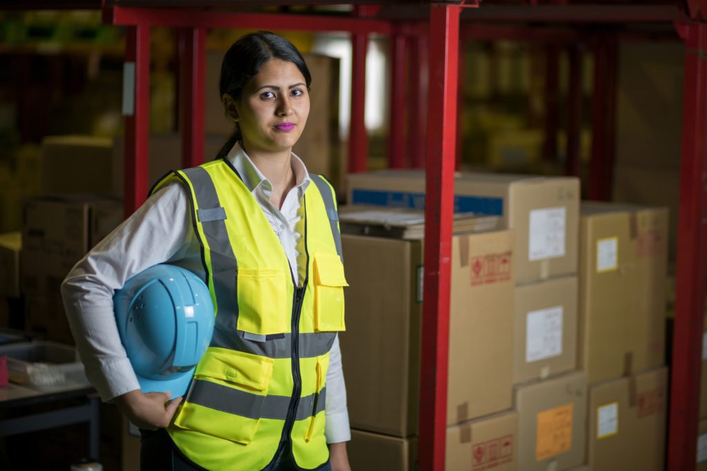 Woman with hard hat and safety vest in warehouse