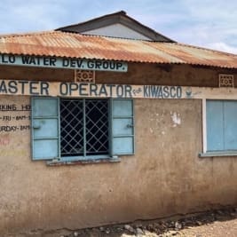 Single story building with sign reading Simba-Kongelo Water Dev. Group