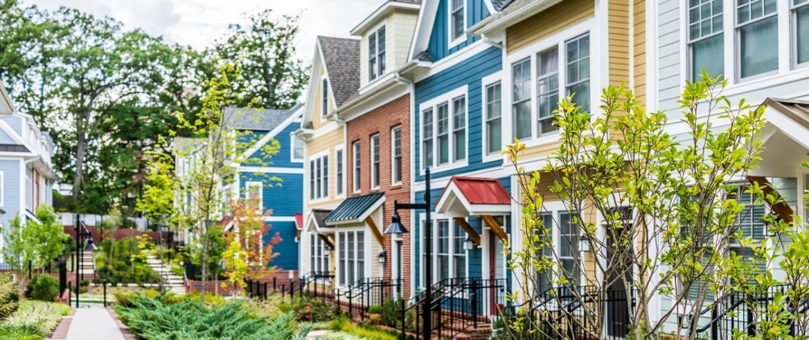 Row of colorful, red, yellow, blue, white, green painted residential townhouses, homes, houses with brick patio gardens in summer r